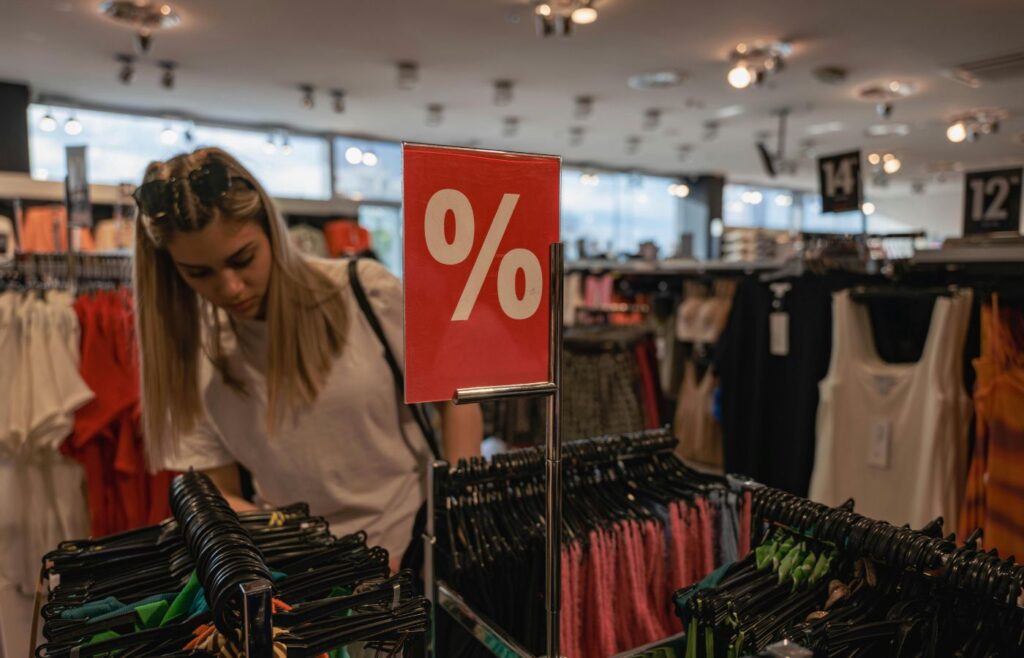 A young woman browses a clothing store during a sale, indicated by a red discount sign.