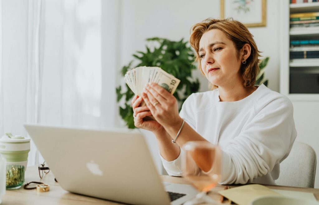 Woman counting money at her desk with a laptop, depicting financial management and success.