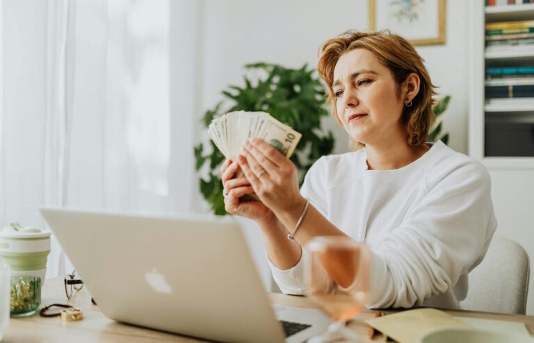 Woman counting money at her desk with a laptop, depicting financial management and success.