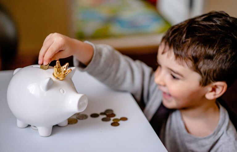 Young boy smiling while saving money in a crowned piggy bank, demonstrating financial responsibility.