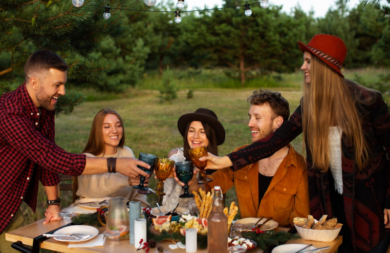 Group of friends toasting at an outdoor fall party with rustic decor and budget-friendly food setup in a forest setting.