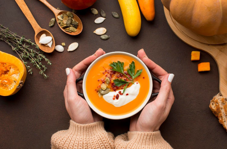 Hands holding a bowl of creamy pumpkin soup topped with sour cream, parsley, and seeds—perfect for budget fall meal prep ideas.
