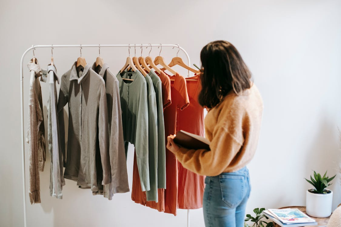 Woman reviewing clothing rack with neutral and warm-toned pieces while building a capsule wardrobe on a budget