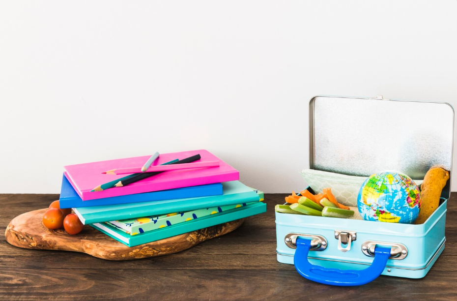 Colorful back to school supplies and healthy lunch packed in a metal lunchbox on a wooden table